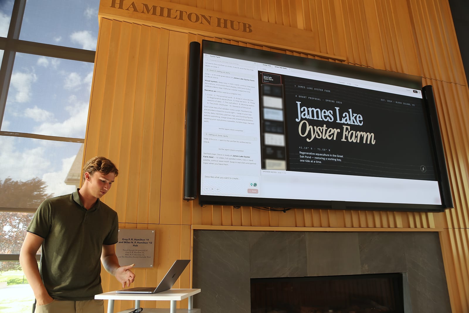 A large screen on a wood-paneled wall shows a design tool with a finished slide deck titled “James Lake Oyster Farm”, a chat panel and slide thumbnails beside it. A laptop sits in front of the screen.